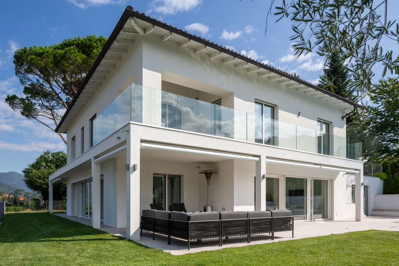 Casa bianca a due piani con balcone in vetro e portico sul giardino
